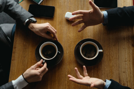 Mãos de homens gesticulando com xícaras de café